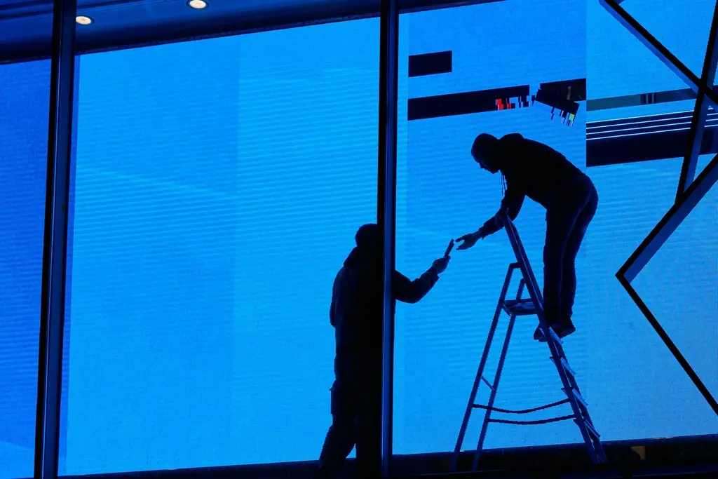 Twee monteurs op een trap aan het werk aan een grote glazen pui