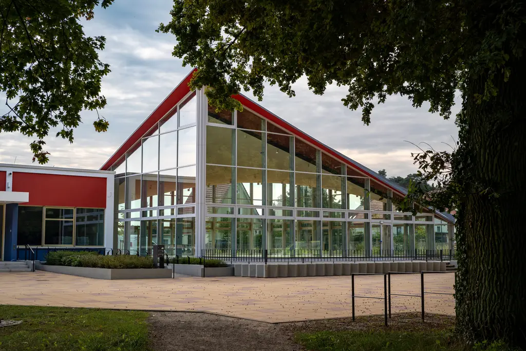 Gebouw met een glazen gevel onder een rood dak tussen de bomen